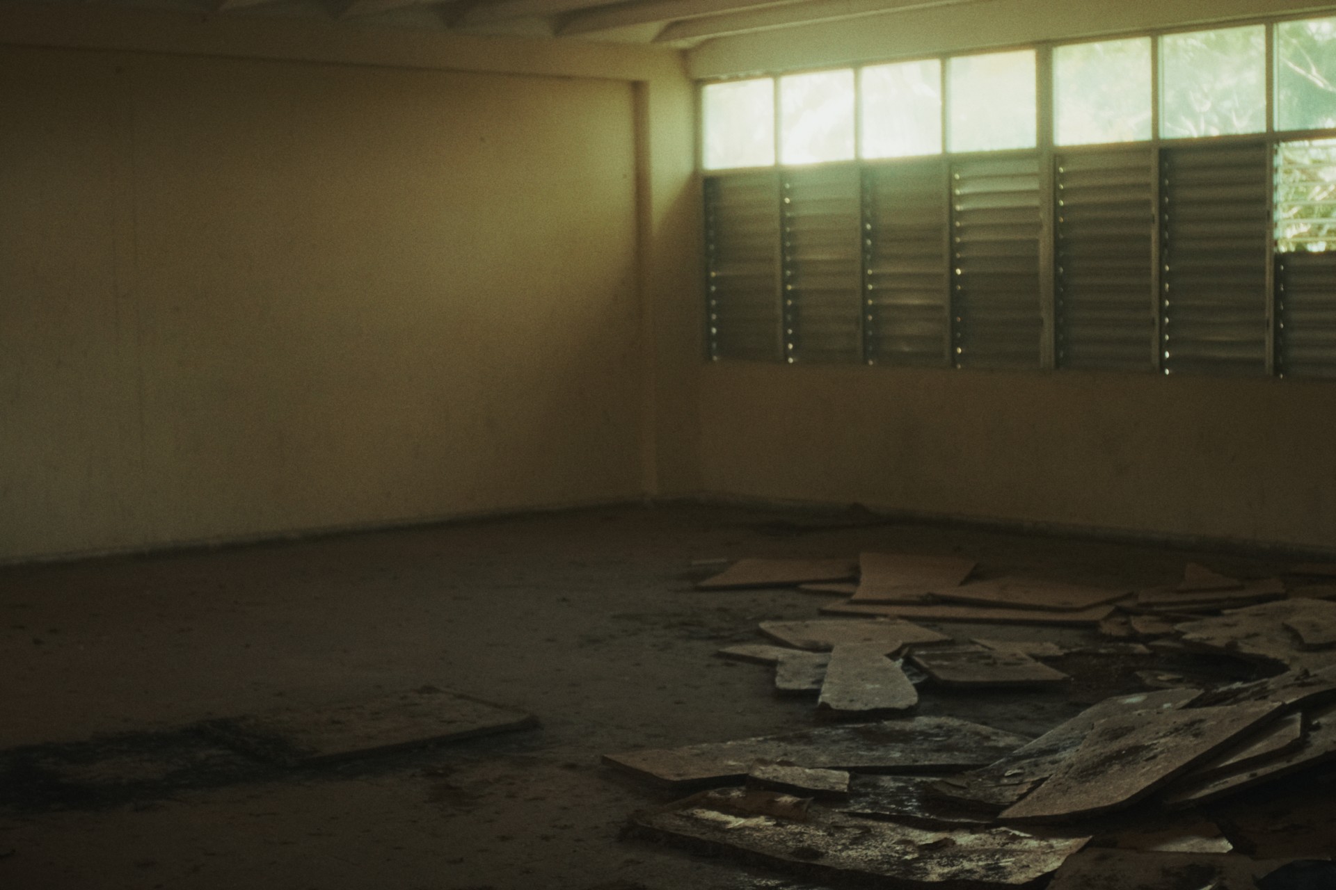 Interior de un albergue estudiantil en Ceiba 1, con restos de materiales en el suelo y ventanas de persiana.